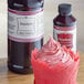a cupcake in a wrapper next to a bottle of strawberry syrup