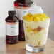 A glass of dessert with a white frosting and fruit in it next to a bottle of LorAnn Oils Mango Super Strength Flavor.