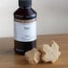 A close-up of a bottle of LorAnn Oils Maple Super Strength Flavor next to white candy.