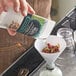 A hand pouring dried fruit into a glass funnel.