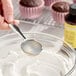 A bottle of LorAnn Oils 4 fl. oz. All-Natural Butter Bakery Emulsion next to a bowl of frosting and cupcakes.