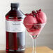 A glass of pink ice cream with cranberries next to a bottle of LorAnn Cran-Raspberry Flavor.