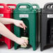 A person's hands holding a green cup and pouring a drink into a green Cambro insulated beverage dispenser.