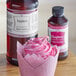 A pink frosted cupcake in a wrapper next to a bottle of LorAnn Raspberry Bakery Emulsion.