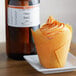 A cupcake with orange frosting in a wrapper on a plate next to a bottle of LorAnn Orange Brandy flavor.