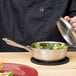 A chef cooking food in a Vollrath stainless steel saucier pan.