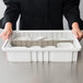 A person holding a clear Metro tote cover over a white container with white bowls and utensils.