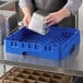 A man using a blue Cambro dish rack to wash a silver tray.