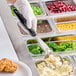 A person in gloves using a Vollrath Jacob's Pride black round portion spoon to serve food.