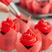 A finger using a pastry bag to pipe red Rich's Buttrcreme icing onto a cupcake.