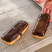 Two chocolate covered pastries on a cooling rack.