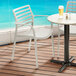 Two Lancaster Table & Seating Allegro beige resin arm chairs on a patio with a table and a glass of beer.
