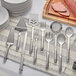 A 10-piece Choice stainless steel serving utensils set on a table with white cloth and silver utensils including a fork, knife, and spatula.