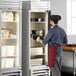 A man in a chef uniform opening a Beverage-Air Vista Series glass door reach-in freezer filled with food.