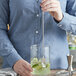 A person mixing a drink with an American Metalcraft stainless steel bar spoon.