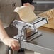 A woman using the Choice Prep electric stainless steel pasta machine to make pasta with a piece of dough.