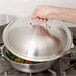 A hand using a Vollrath high domed lid to cover a pan of food.