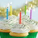 A cupcake with white frosting and rainbow sprinkles with a rainbow spiral candle on top.