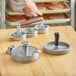 A man using a Choice hamburger press to make burgers on a wooden surface.