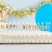 A close-up of a birthday cake with gold "Happy Birthday!" candles on top.