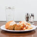 A Carlisle white melamine plate with pasta and meatballs on a table.