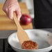 An American Metalcraft wood spatula cooking a hamburger in a pan.