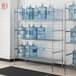 A metal wire shelf with three shelves holding water jugs.