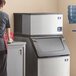 A woman standing next to a Manitowoc water cooled half dice cube ice machine.