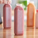 A person holding a customizable tall square PET clear juice bottle filled with pink liquid.