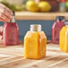 A person pouring orange juice into a customizable square PET juice bottle.