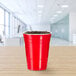 A red Solo plastic cup on a table with brown liquid in it.