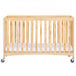 A natural wood full size folding crib with wheels.