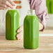 A person holding a customizable square clear PET juice bottle filled with green liquid.