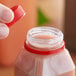 A hand holding a red plastic bottle of juice with a red tamper-evident cap.