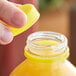 A hand with a yellow unlined tamper-evident cap over a bottle of juice.