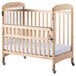 A natural wood crib with a white sheet on the mattress.