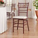 A mahogany wood Chiavari chair with an ivory cushion.