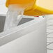 A yellow container pouring water into a stainless steel mop sink.