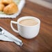 A CAC Collection bright white porcelain coffee cup on a table with coffee and a spoon.