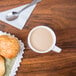 A CAC Collection white porcelain coffee cup filled with coffee on a table with croissants and a spoon.