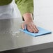 A person cleaning a counter with a blue ChoiceHD foodservice wiper.