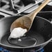 A wooden spoon with white liquid on it stirring a pan.