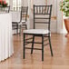A black wood Chiavari chair with a white cushion.