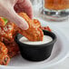 A hand dipping a piece of chicken into a black Acopa ramekin of sauce.