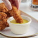 A person dipping a fried chicken strip into a white Acopa fluted ramekin of sauce.