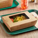 A Kraft paper take-out container with food inside on a table.