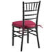 A Lancaster Table & Seating black wood Chiavari chair with a wine red cushion.