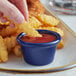 A person dipping a french fries into a blue Acopa melamine ramekin with ketchup.