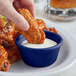 A person dipping a piece of chicken into a blue Acopa fluted ramekin of sauce.