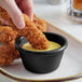 A person dipping a chicken finger into a black Acopa ramekin of sauce.